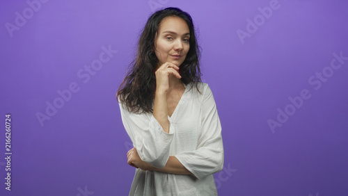 Konstfotografi Woman with hand to chin and folded arm in studio purple backdrop, thinking gesture and subtle smirk; contemplative reflection