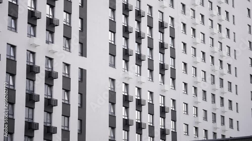 Minimalist urban architecture with clean white walls dark gray vertical accents. Symmetrical grid of windows small balconies under even daylight. Monochrome palette evokes calm order