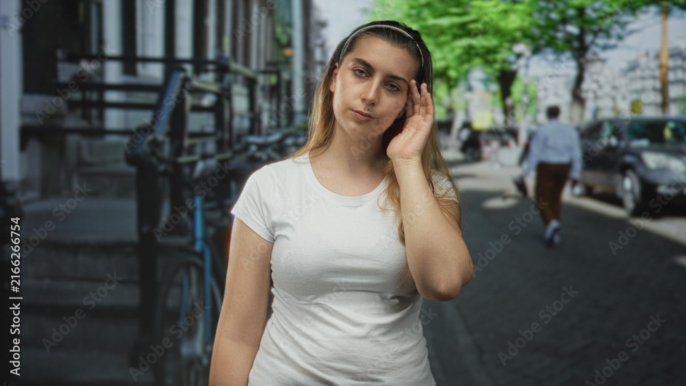 Fototapeta premium Woman with hand to temple and closed eyes on a city street with bicycle rack nearby; contemplation solitude.