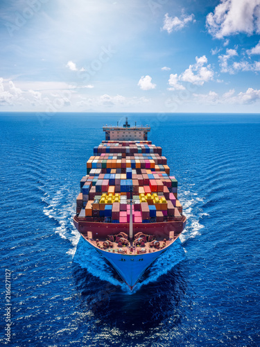 Aerial front view of a large container cargo carrier ship cruising with speed over the ocean as a industrial transport concept