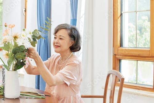 Fotografie Senior woman arranging flowers in a bright home interior