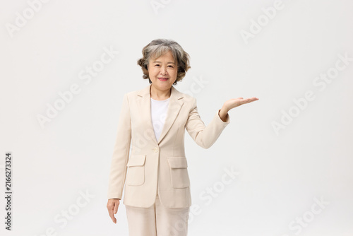 Canvas Print Smiling senior Asian woman in beige suit presenting with open palm