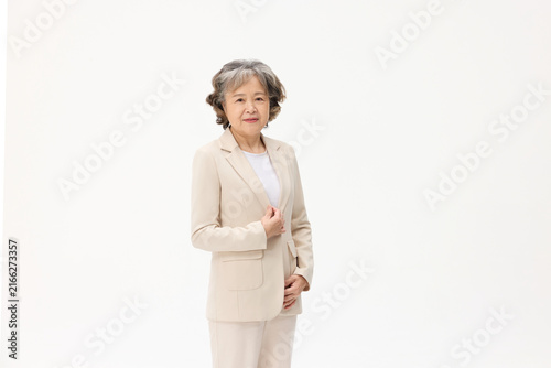 Fotografía Elderly Asian businesswoman in beige suit standing on white background