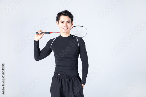 Smiling young man holding badminton racket in athletic wear
