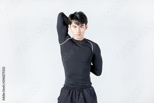 Athletic young man stretching shoulder in black sportswear studio portrait
