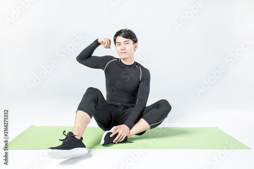 Athletic man stretching on exercise mat and flexing arm indoors