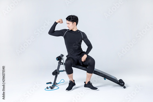 Athletic man flexing arm while sitting on workout bench in studio
