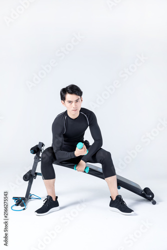 Young man lifting dumbbells on exercise bench in studio