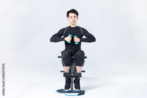 Young man doing seated dumbbell workout on exercise bench in studio