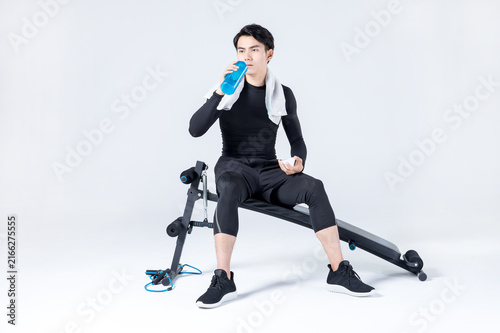 Young athletic man resting on exercise bench and drinking water after workout