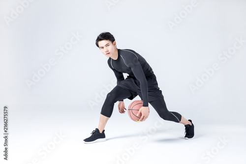 Athletic young man dribbling basketball in studio