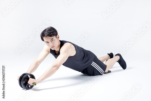 Young man performing ab roller kneeling exercise in white studio