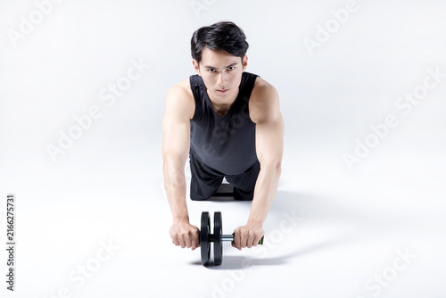 Young man performing ab wheel rollout exercise in white studio