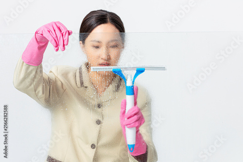 Foto Female cleaner washing glass with squeegee and pink gloves indoors