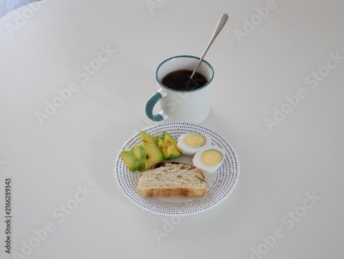 Quadro su tela Breakfast plate with avocado, hard-boiled eggs, bread and coffee mug on a bright