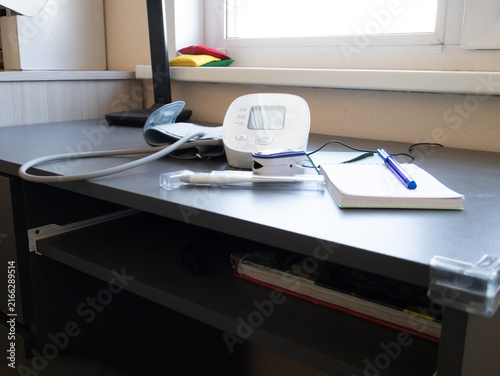 Foto Digital blood pressure monitor with cuff sits idle on a tidy desk by a window in
