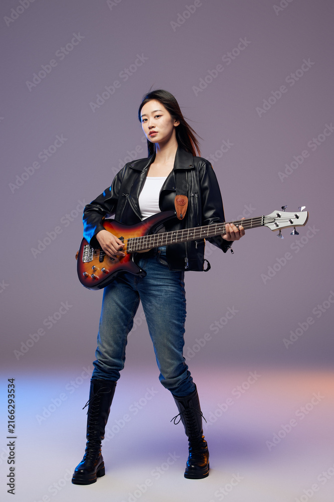 Fototapeta premium Confident young woman holding electric bass guitar in studio
