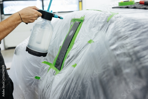 Cuadro en lienzo Hand spraying protective coating on masked car body during paint preparation ins