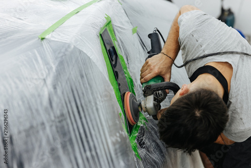Foto Technician sanding car body during repair work, using power grinder on masked ve