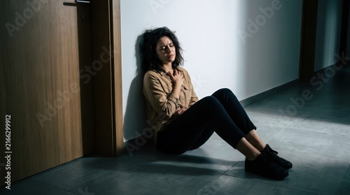Anxious woman sitting on the tiled floor of a house hallway during a panic attack.