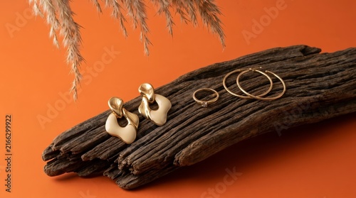 Luxury jewelry set on a textured piece of wood with decorative pampas grass against orange.