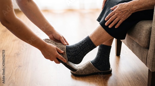Caregiver helping elderly woman put on comfortable slippers at home, senior care assistance, nurse aiding old lady with footwear, compassion and support for aging parents