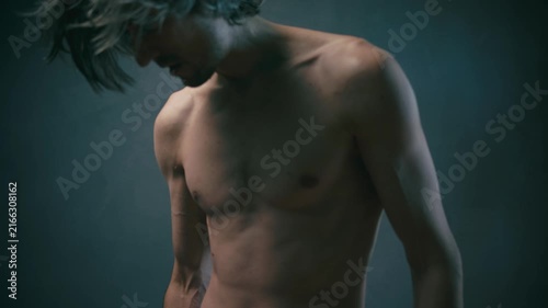 pressure of circumstances Close-up portrait of a slender young man with long hair in motion, hand near chest, low-key studio lighting against a dark blurred background
