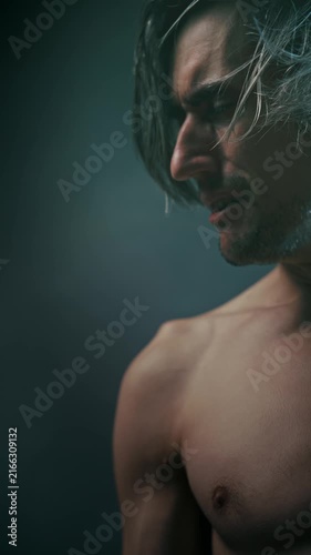 suffering bitterness pain Side-profile portrait of a shirtless young man with long hair in dramatic studio lighting, highlighting defined facial and body contours against a dark background