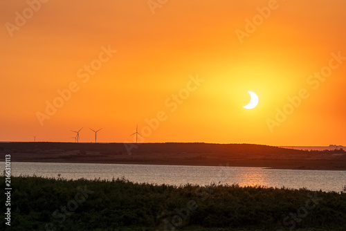 Crescent eclipsed sun setting over wind turbines at San Salvador reservoir, Spain.