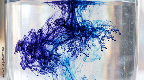 Indigo ink spreading in clear water. Abstract blue liquid cloud swirling in a glass.