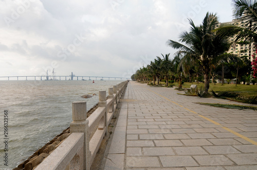 Scenic pedestrian promenade along Couple Road (Lovers' Road) in Zhuhai, Guangdong, China, overlooking the coastal waters with a distant view of the Hong Kong-Zhuhai-Macau Bridge.