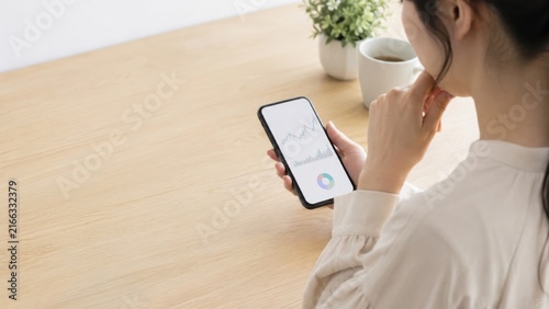 Obraz na płótnie スマートフォンで株価チャートを確認する日本人女性の資産運用