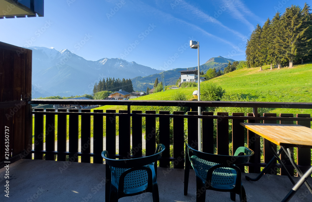 Fototapeta premium cozy wooden balcony with comfortable lounge chair overlooking scenic green mountains