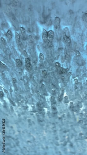 Thick blue soap foam and water droplets slide down a car windshield during an automated car wash cycle, creating an abstract liquid texture.