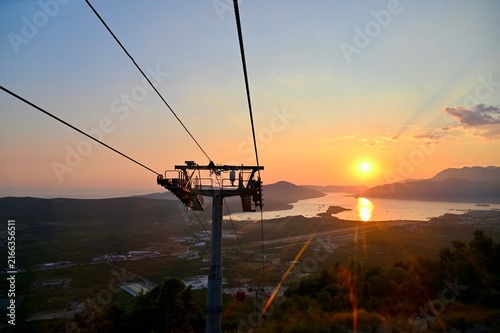 Cuadro en lienzo A sunset panorama featuring a central cable car tower, taut cables, the sea, mountains, and city lights below