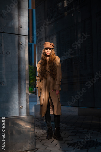 Canvas Print Elegant young woman in tan trench coat and brown newsboy hat standing beside sle