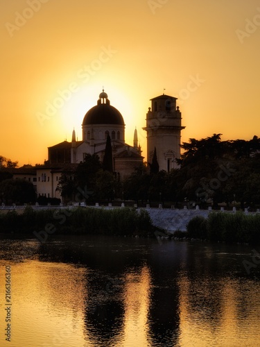 Canvas Print Golden sunset silhouette of San Giorgio in Braida church in Verona, Italy, with warm orange sky and reflections on the Adige River