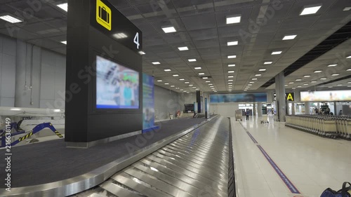 continuous flow Baggage claim conveyor belt in an airport terminal with metallic surface reflecting belt plate without luggage bag at arrival hall area in airport with sign board of flight number