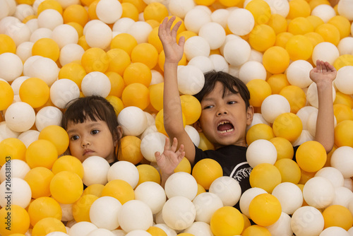 Two Happy Asian Children Having Fun Submerged in Yellow and White Ball Pit