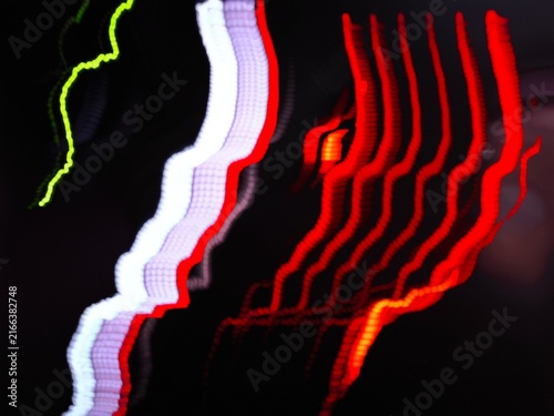 Abstract long exposure light trails with wavy red white and green glowing lines on black background