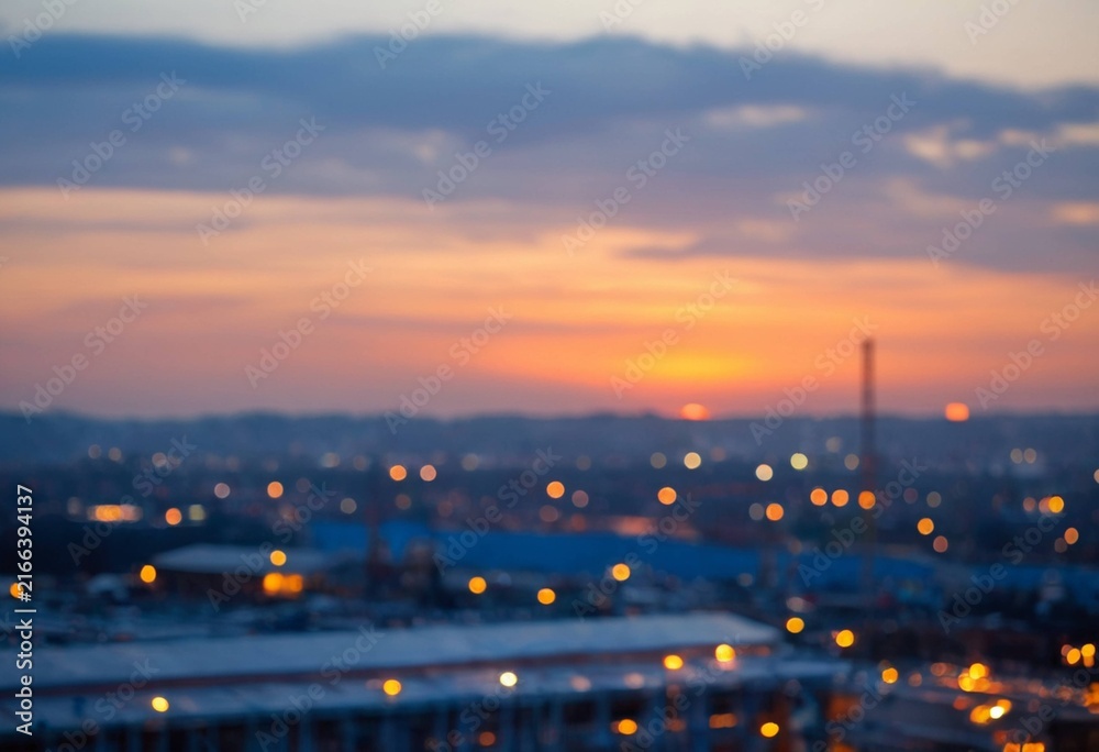 Fototapeta premium Blurred Cityscape at Sunset with Warm Sky and Bokeh Lights