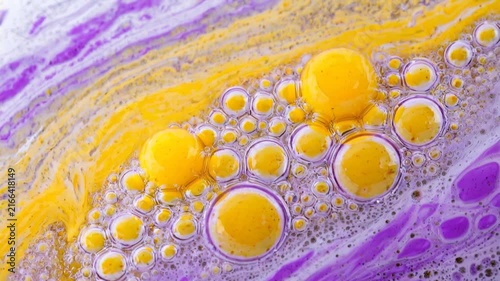 Macro shot of vibrant yellow and purple paint swirling smoothly with floating liquid bubbles in a mesmerizing, colorful abstract fluid movement.