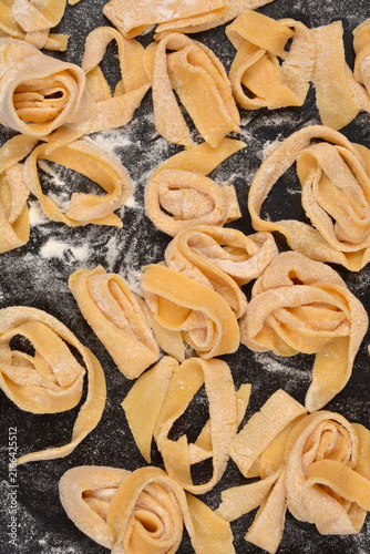 Fotografie A top down full frame view of fresh raw homemade fettuccine pasta nests sprinkled with white flour on a dark surface