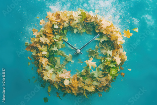 Clock surrounded by fresh green leaves splashing on a blue background.