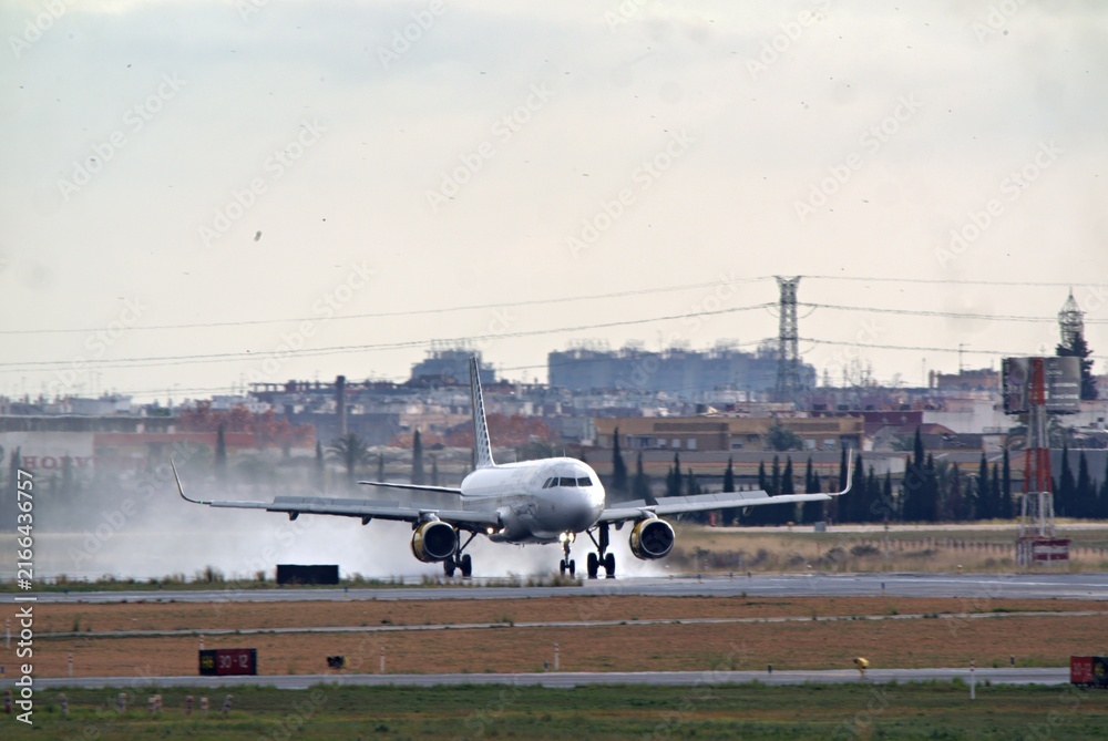 Fototapeta premium Airplane landing on airport runway with jet engine exhaust and city skyline in distance