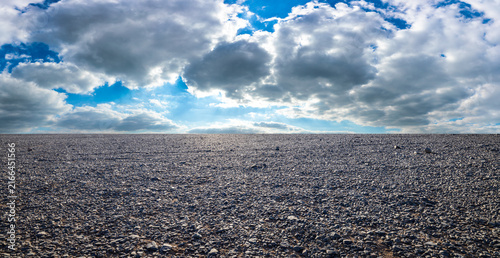 Foto Vast gravel plain under dramatic blue sky with white clouds and sunlight in Xinj