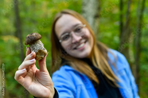 A smiling woman holds a freshly picked brown birch bolete mushroom in an autumn forest. The image represents wild mushroom foraging, outdoor recreation, and organic food gathering.