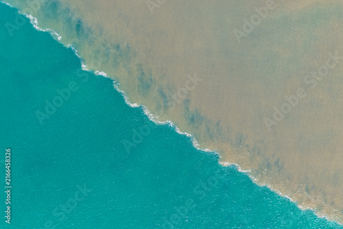 Aerial downward view of brown floodwaters flowing into the ocean and meeting clear turquoise seawater, creating a striking boundary of contrasting colours, sediment and swirling water patterns 