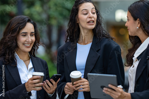 фотографія A team of three Hispanic businesswomen in matching dark suits, absorbed in the numbers on screen, hold an impromptu walking meeting over a tablet, a female leadership theme