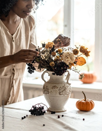 Woman Arranging Autumn Flowers and Berries in Antique Vase for Seasonal Decor